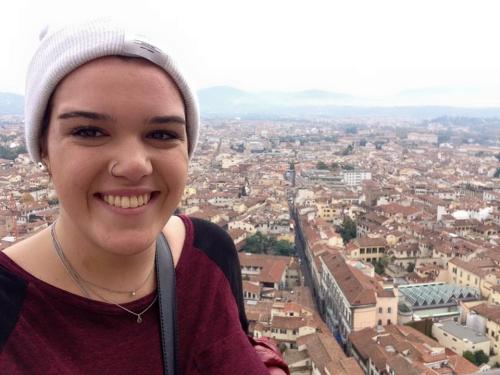 Pia Wright smiles, wearing a beanie, with a city in the background.