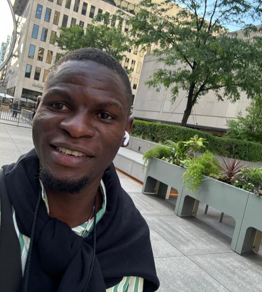 A selfie of a man in a green shirt and dark sweater standing in front of a building