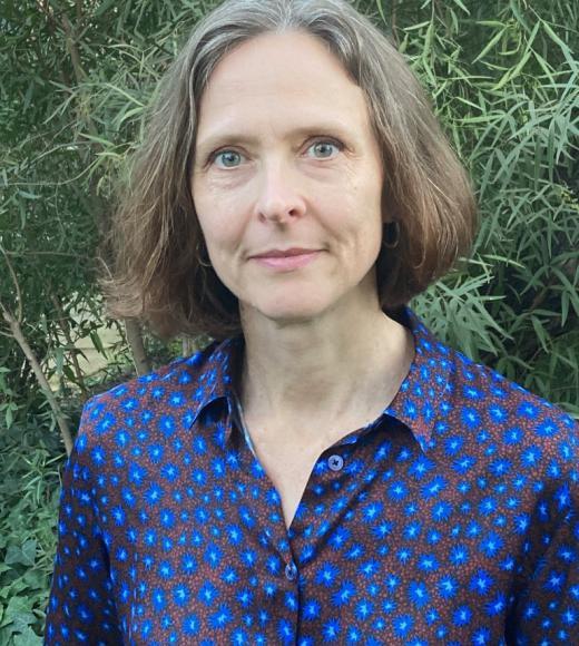 Woman in a patterned blue blouse, posing in front of greenery
