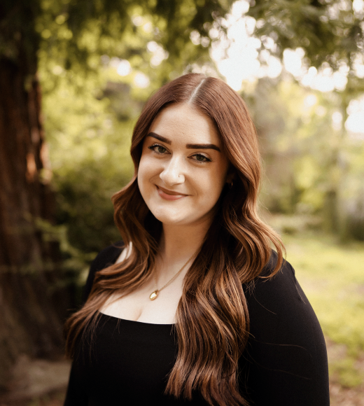 A woman with brown hair, a tree in the background.