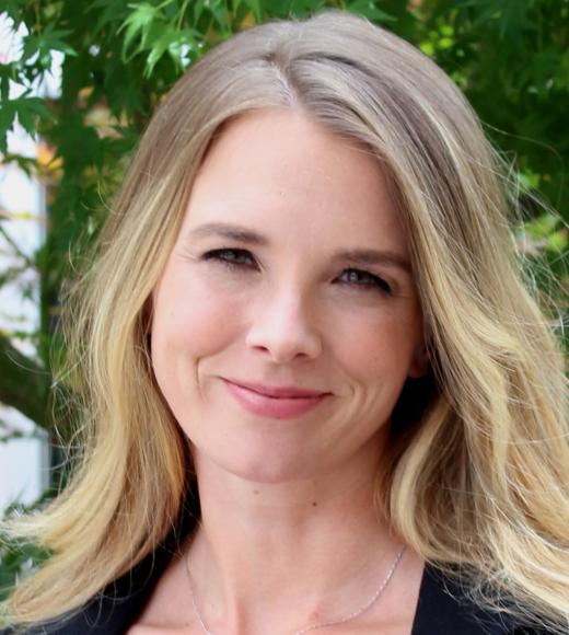 A woman with blonde hair in front of greenery