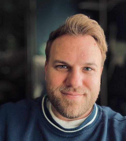 A photo of a man with a beard in a blue sweater