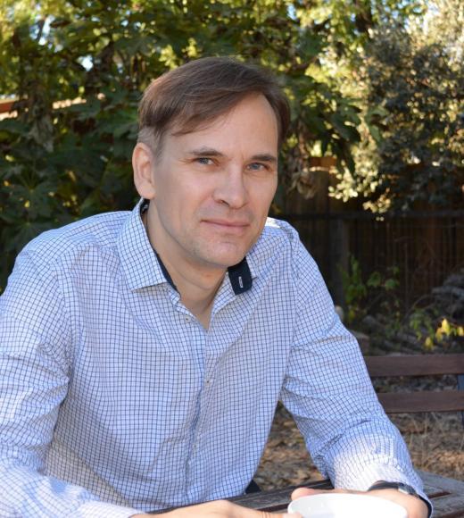 Man in pale blue shirt, posing in front of greenery