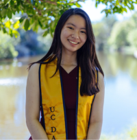 Smiling young woman wearing a yellow graduation stole standing by a lake