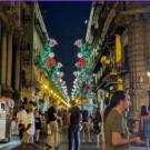 An Italian street with decorative lights and a crowd of people