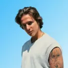 a man wearing a white vest against a blue background.