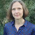 Woman in a patterned blue blouse, posing in front of greenery