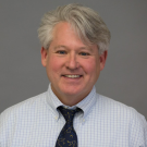 Man in shirt and tie, posing in front of a gray background